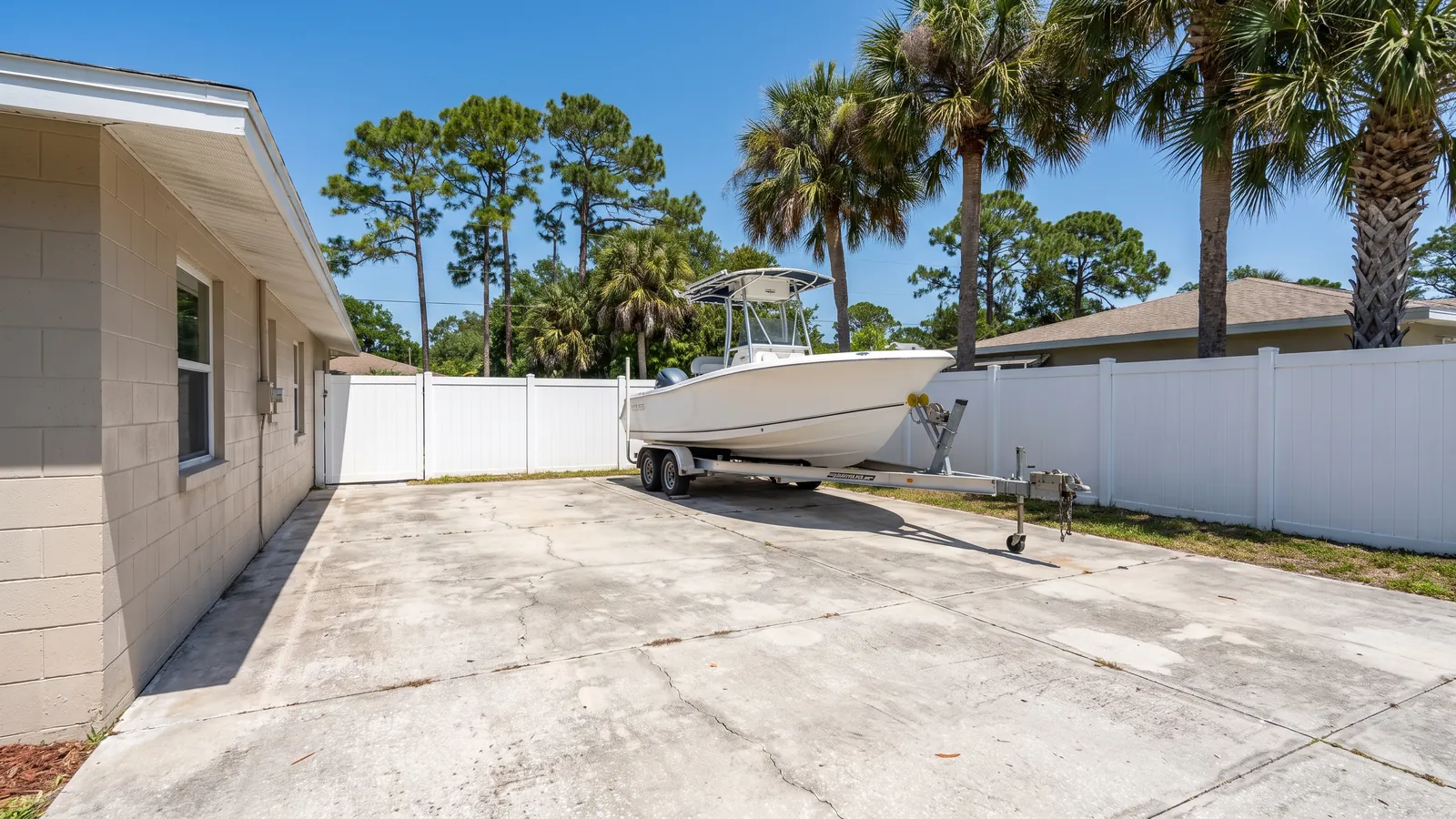 Thick reinforced concrete side-yard pad with a center-console boat on a trailer parked on it beside a vinyl fence